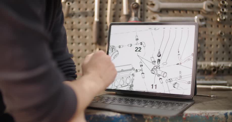 A person in the garage using a laptop on a workbench with a wall and tools in the background
