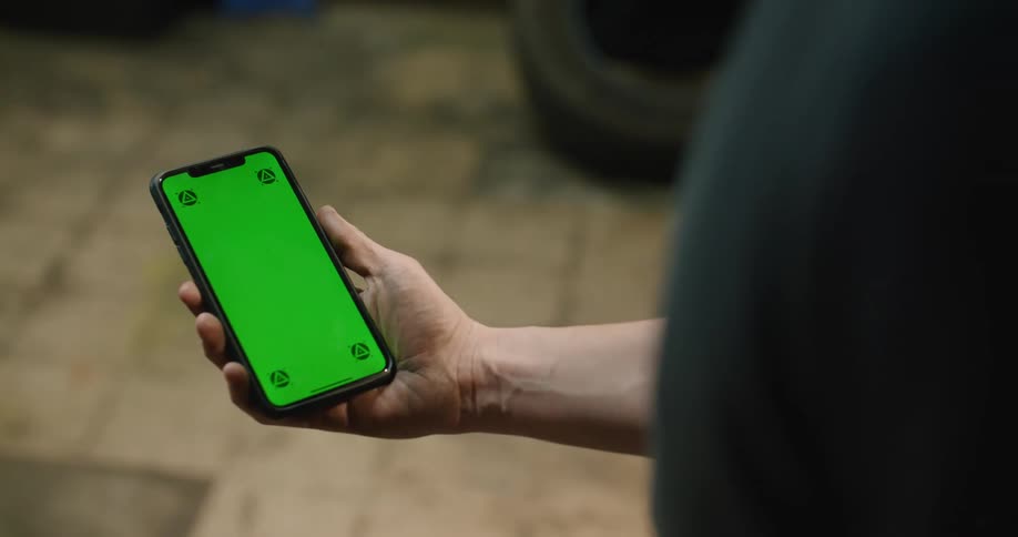 A man holds a smart phone with a green screen