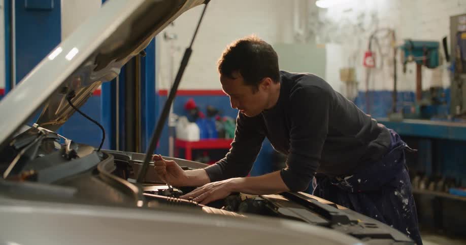 A male mechanic working under the hood of a car in an auto body shop