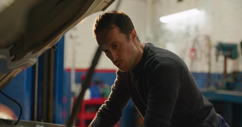 A man in a garage working with a tool under the hood of a vehicle with a wall in the background