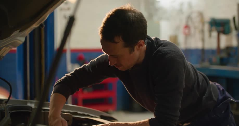 Mechanic working along in garage uses hand tool while working on car engine