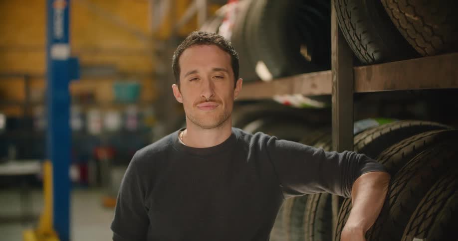 A man stands beside a large shelf with multiple tires