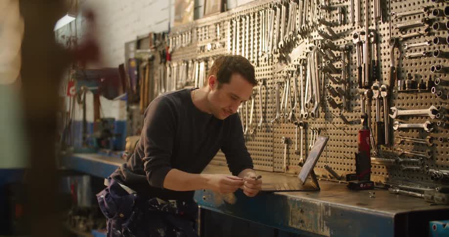 A man in a garage using a laptop with a wall and tools in the background