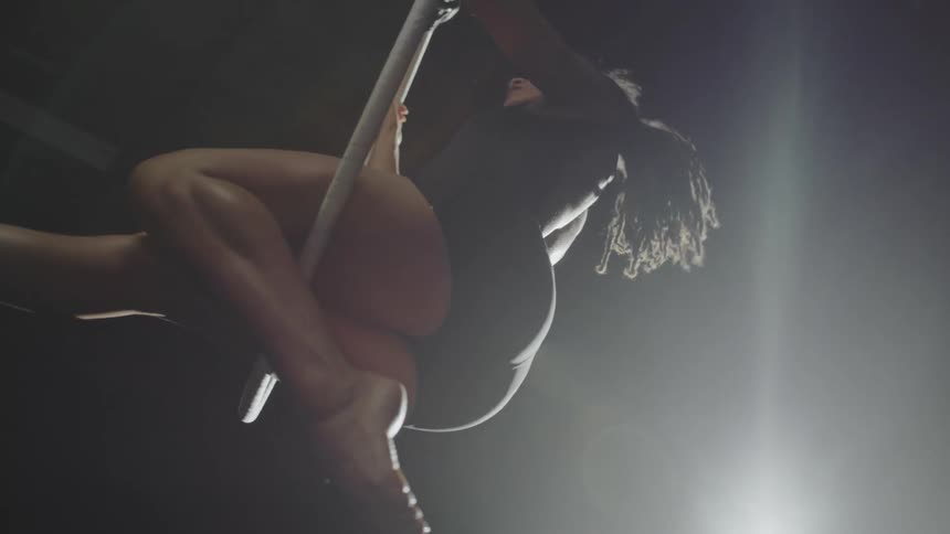 An aerial acrobat flips down from above a hoop and holds a pose