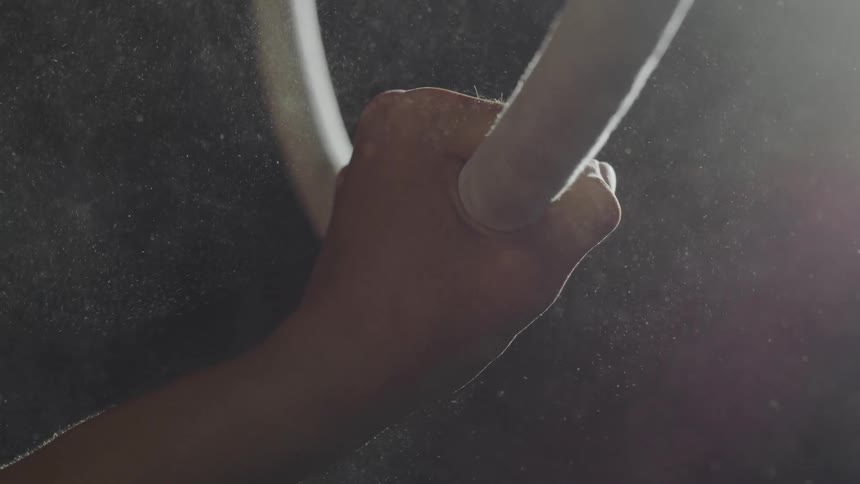 Gymnast grabs large suspended acrobatic ring releases cloud of dust into air from powdered hand