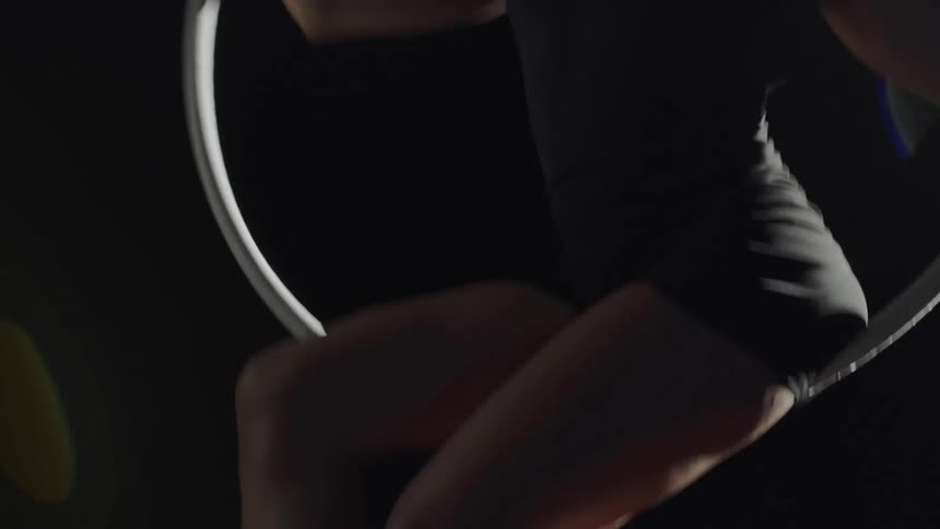 A female acrobat spins around while seated on a rotating hoop