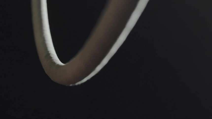 Female acrobat grasps white hoop against dark background