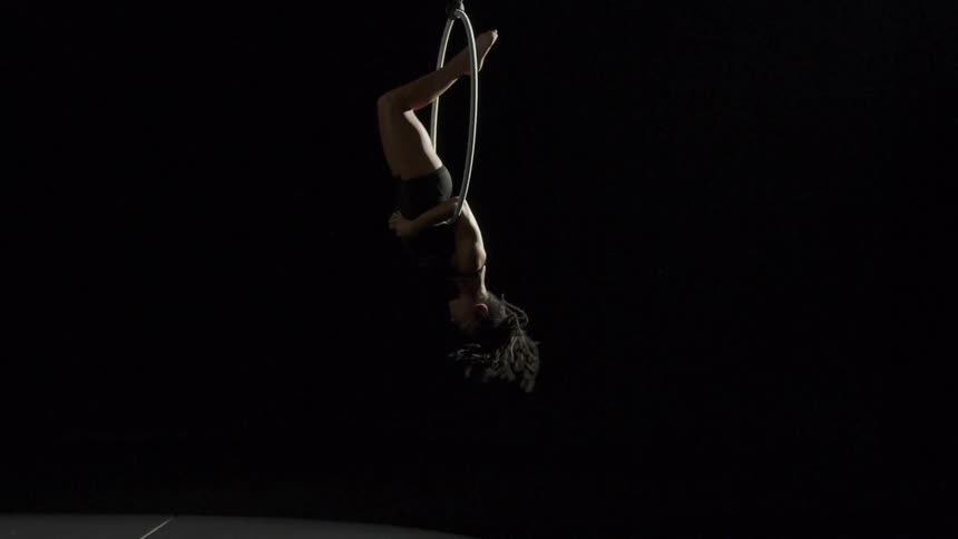 A teenage girl performing acrobats flips through a ring suspended in the air