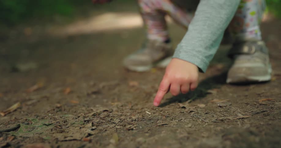 A toddler crouched outside and pointing at the dirt ground