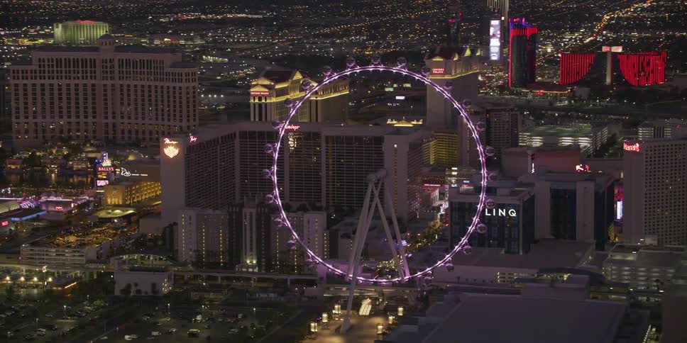 An aerial view of a lit up ferris wheel and skyscrapers in a large city at night
