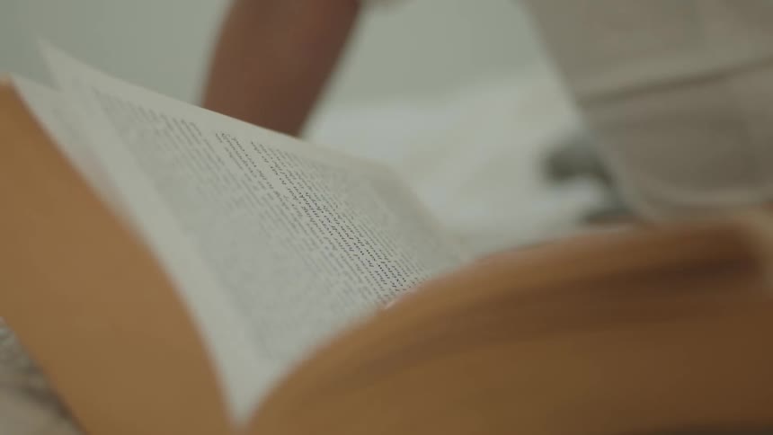 A woman turns the page as she reads a book while sitting indoors
