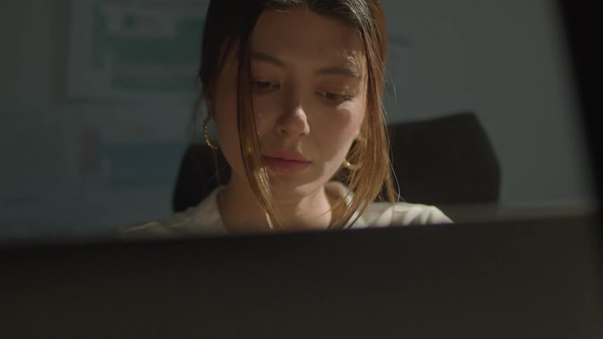 A young woman types on a laptop while sitting at a desk