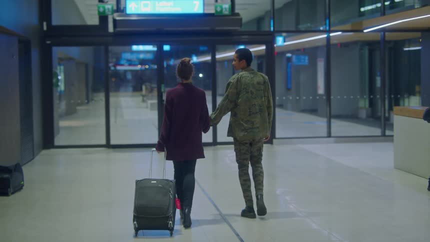 A couple walks hand in hand through an airport towards a door