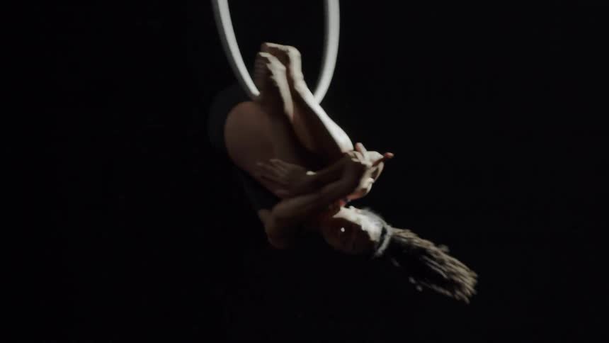 A woman extends her leg while spinning on a ring suspended in the air