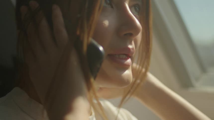 A woman talks on her smartphone while standing next to an angled window