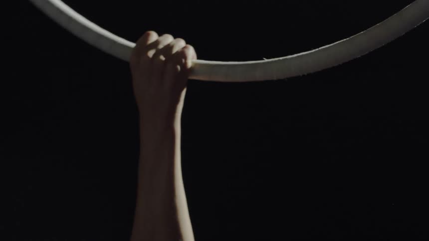 A woman spins from a ring suspended in the air and drops one hand from holding on