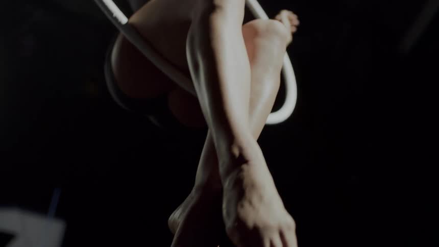 A woman does a flip and sits on the hanging ring