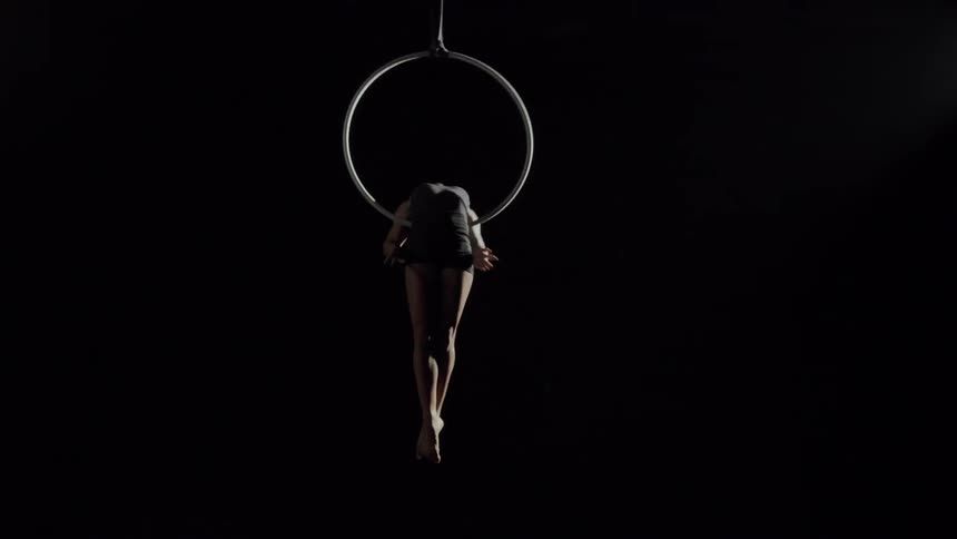 A young acrobat leans back as she spins around on a ring suspended in the air