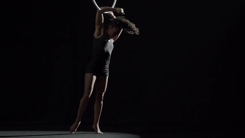 A female performer spinning on a suspended hoop and performing tricks