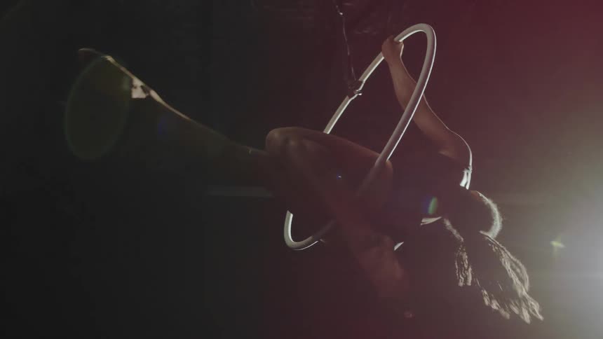 Young fit strong woman doing acrobatic stunts on a ring suspended from the ceiling