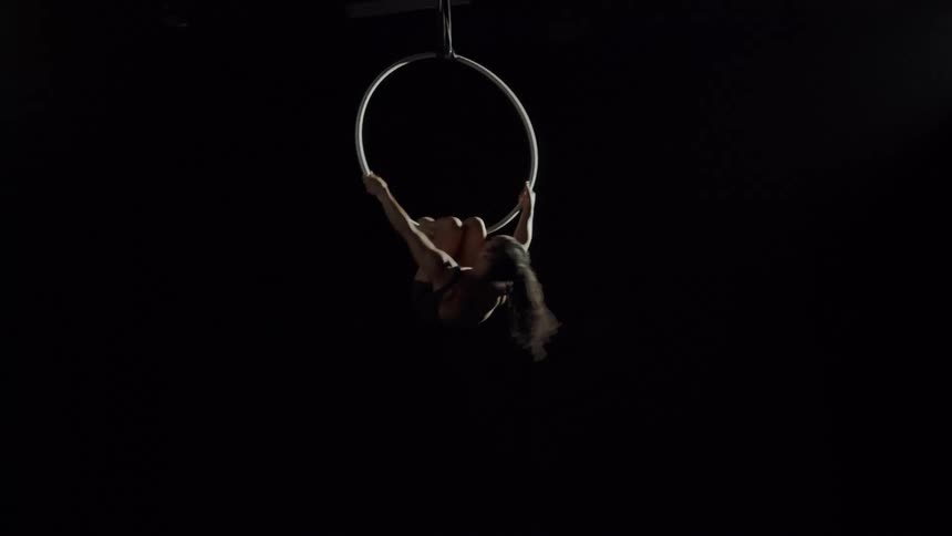 A teenage girl performing acrobats hangs from a spinning ring and flips her body inside the ring