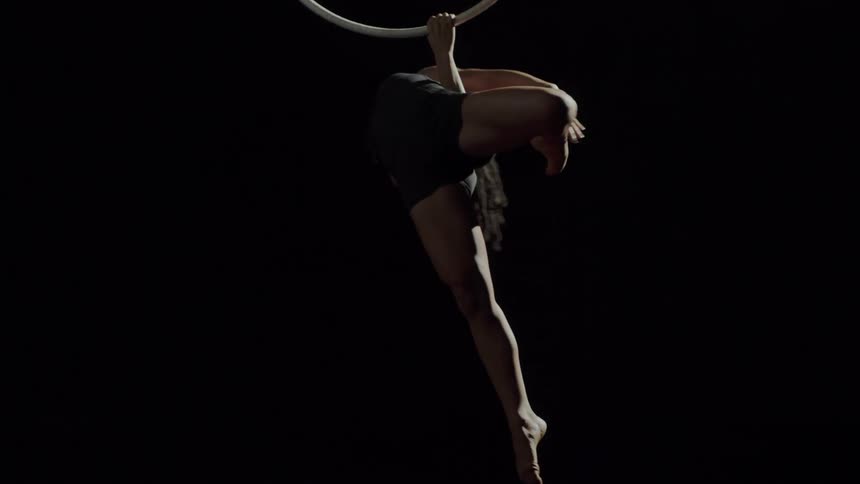 A woman in a room hanging on a gymnast ring with a wall in the background