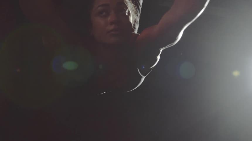 An aerial acrobat spins and hangs from a hoop as a light shines on her