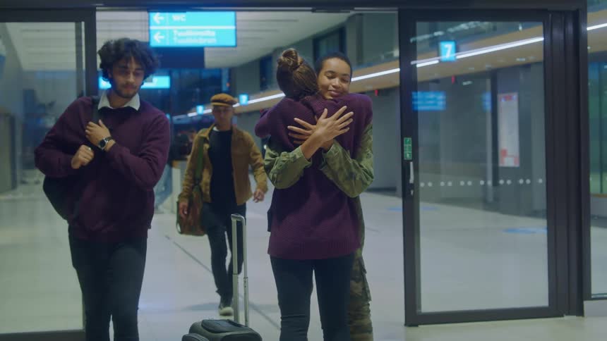 A woman in military gear leaving an airport and getting hugged