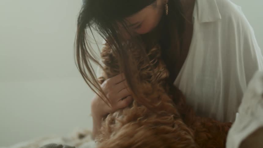 A woman is cuddling with her dog on the bed