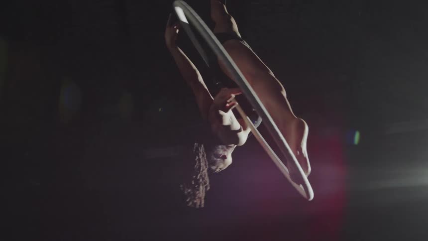 A female acrobat spinning on a suspended hoop while doing tricks