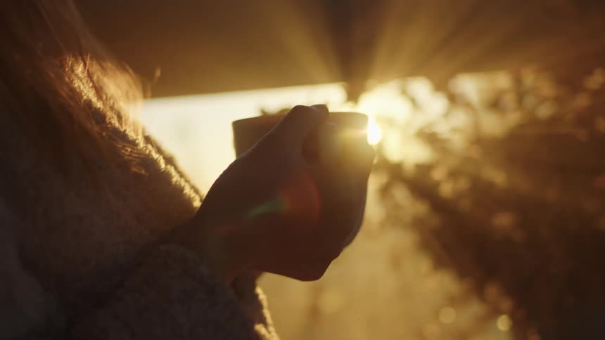 Sunlight shining behind a woman holding a mug of coffee at sunrise
