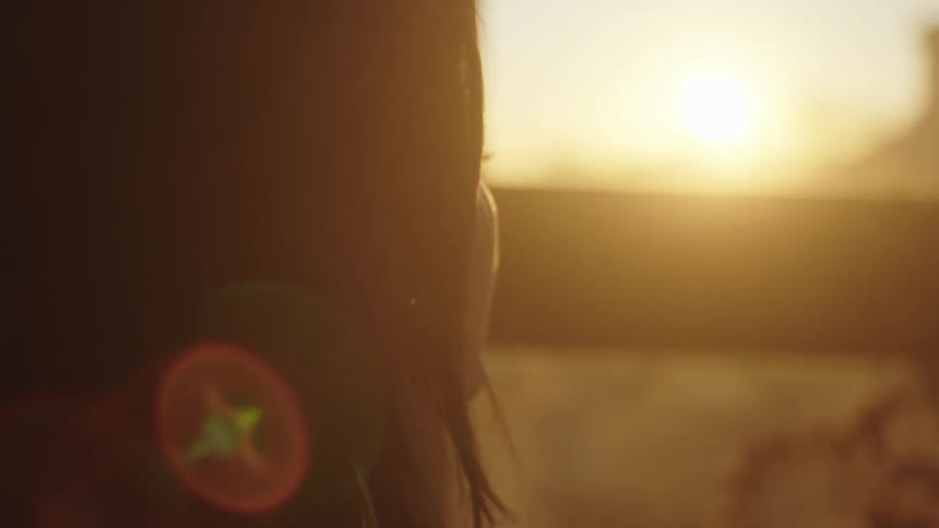 Woman looks out window toward sun glaring from sky