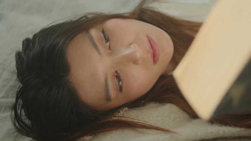 A woman in a room laying in bed reading a book