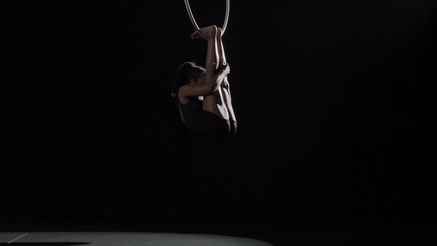 Young fit muscular woman doing acrobatics hanging from a ring