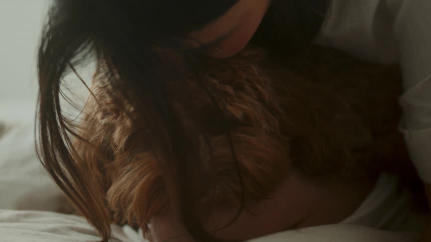 Girl sitting in the bed kisses a brown fluffy dog on the forehead