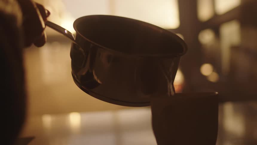 A person is pouring hot water from a pan into a mug