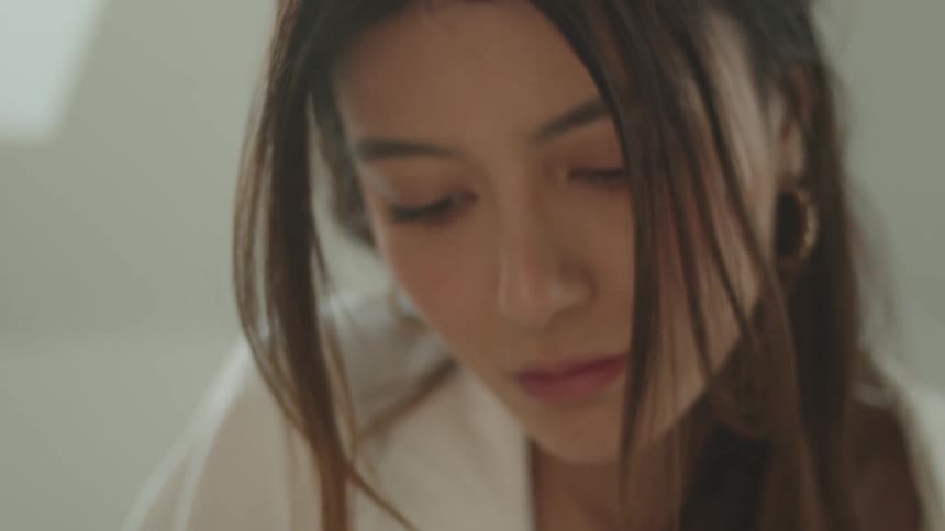 A woman with a ring sitting on a bed in a room reading a book with a wall in the background