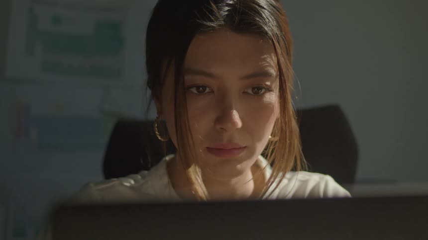 A woman sits at a desk while looking at a computer screen as she types