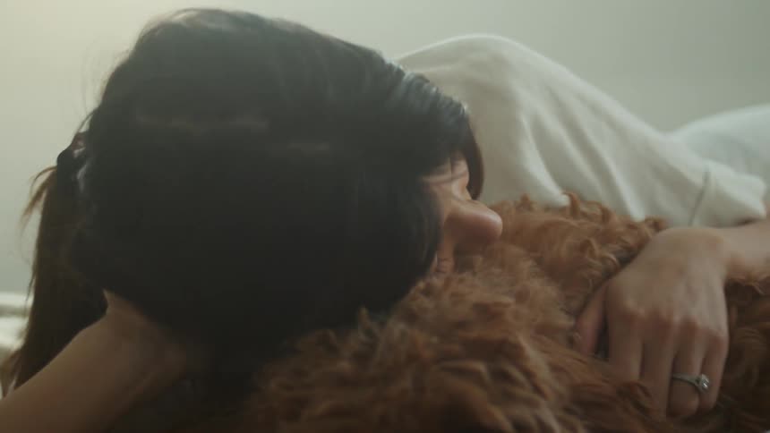 A woman in a bedroom laying in bed next to a dog with a wall in the background