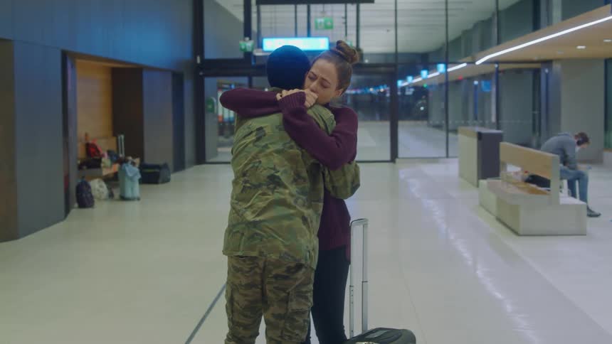A woman hugging a servicemember in camouflage at an airport