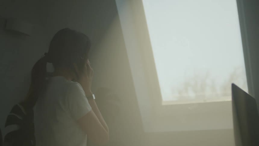A woman picking up and answering a phone from a desk next to a sunny window