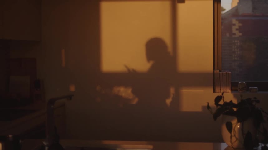 Sunlight casts a womans shadow against an apartment wall as she stands and texts