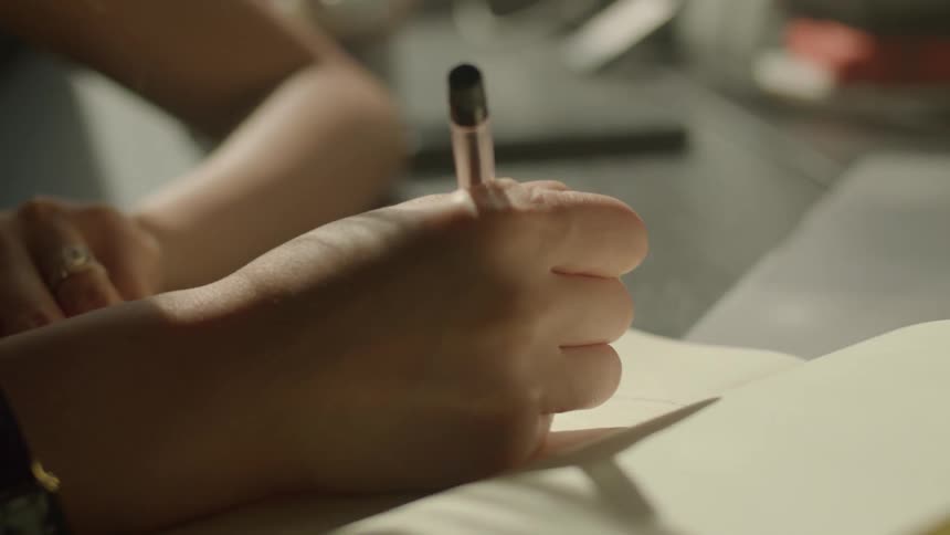 Woman handwriting with a pen on a notebook over a desk