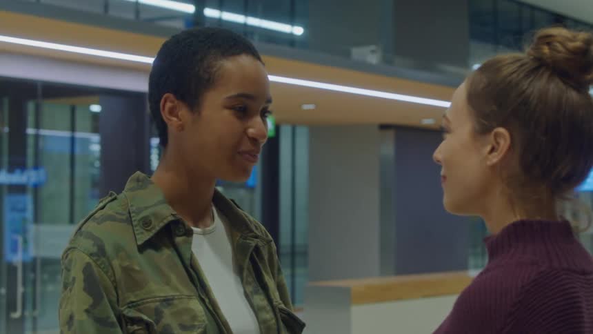 Women stare into each others faces smiling standing in transit terminal