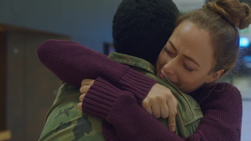 Woman cries as she greets woman wearing a military jacket with a hug while standing in terminal