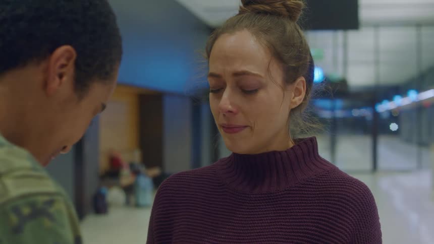 A woman cries as she stands in front of a man in an airport