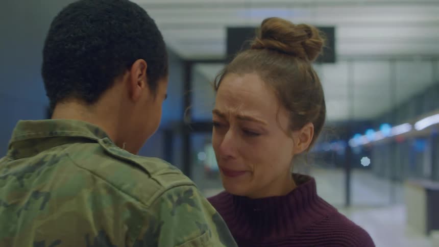 Woman cries and hugs soldier wearing military fatigues in terminal