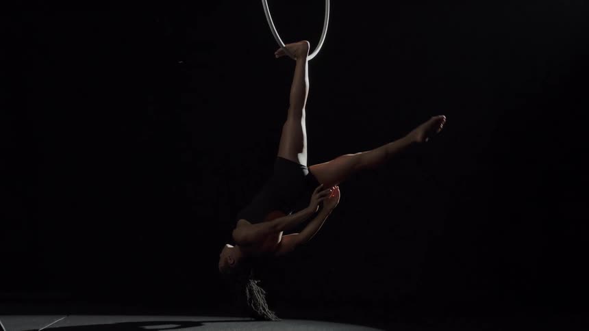 A female acrobat hangs upside down from a large suspected hoop while she poses