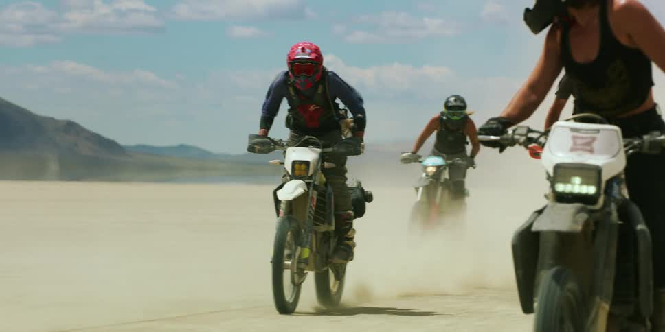 A group on motorcycles swerve as they ride in a desert