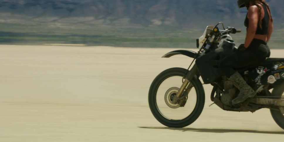 A man and woman are racing motorcycles across a salt flat